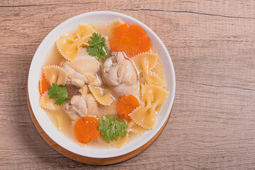 Wall Mural - Macaroni soup with chicken thighs in clear broth with carrots.on an rustic old wood background.