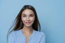 Headshot Of Tender Girlfriend With Pleasant Appearance, Smiles Tenderly, Arranges Spa Salon Relaxation Weekend, Satisfied After Cosmetic Procedures, Has Healthy Fresh Skin, Isolated On Blue Background
