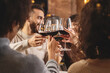 © Lomb - Group of young friends toasting with red wine for celebration at restaurant - young adults clinking raising wineglasses - people friendship and lifestyle concept
