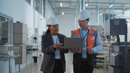Poster - Two Professional Heavy Industry Engineers Walking at a Factory in Safety Uniform and Hard Hats, Discussing Work on Laptop Computer. Asian Specialist and African American Technician at Work. Handheld.