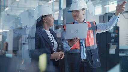 Aufkleber - Two Professional Heavy Industry Engineers Wearing Safety Uniform and Hard Hats Discussing Factory Work on Laptop Computer. African American Specialist and Asian Technician at Work.