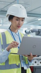 Poster - Vertical Screen: Happy Asian Female Engineer in Hard Hat Standing and Using Laptop Computer at Electronic Manufacturing Factory. Technician Thinking About Daily Tasks and Working on Production Plan.