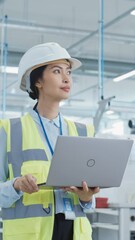 Poster - Vertical Screen: Happy Asian Female Engineer in Hard Hat Standing and Using Laptop Computer at Electronic Manufacturing Factory. Technician Thinking About Daily Tasks and Working on Production Plan.