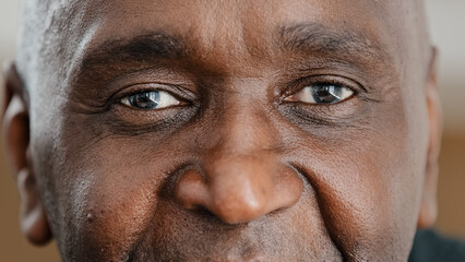 Close up part male face happy elderly African American man smiling with friendly dark black eyes. Handsome mature senior citizen with wrinkles looking blink wink with eye friendly eyesight good vision