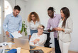 © Renata Hamuda - Multi-ethnic co-workers around a young woman in a wheelchair pointing at a laptop screen while leading a business meeting in the office