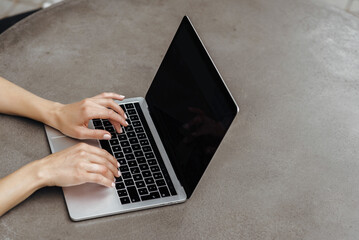 two hands of woman typing on the keyboard of the screen of the laptop on the grey table, working outdoors