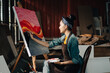 © saksit - Asian Female Artist Draws create art piece with palette and brush painting at studio.