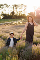 Wall Mural - Pretty woman in a dress and hat walks with her son by the hand in a lavender field