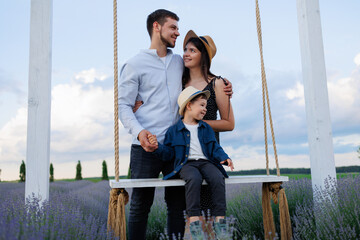 Wall Mural - Happy married couple swings their son on a rope swing in a field