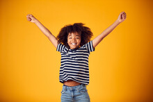 Studio Shot Of Energetic Boy Jumping In The Air With Outstretched Arms Against Yellow Background