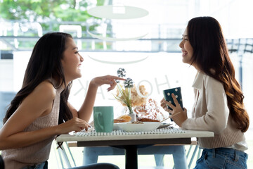 Two young Asian women friends talking at a coffee shop