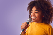 Studio Shot Of Boy Singing Karaoke Into Microphone Against Purple Background