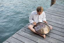 Overhead View Of Man Playing Hang Drum On Wooden Pier Above River In Venice.