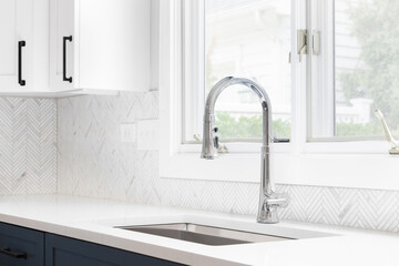 Wall Mural - A kitchen sink detail shot with blue and white cabinets, herringbone tile backsplash, and a chrome faucet in front of a window.