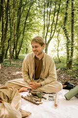 Smiling man sitting near aroma stick and teapot during tea ceremony in forest.