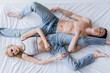 © LIGHTFIELD STUDIOS - Top view of young couple in jeans lying on bed on grey background.