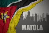 Fototapeta  - abstract silhouette of the city with text Matola near waving colorful national flag of mozambique on a gray background.