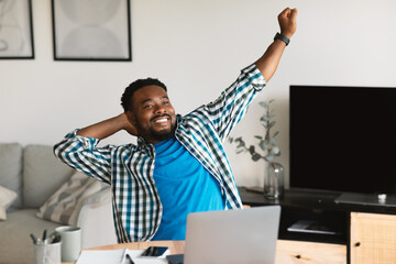 Wall Mural - Relaxed Black Man Stretching Hands Sitting At Laptop At Home