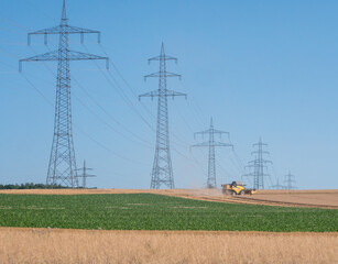 Poster - Mähdrescher mäht ein Feld in der Nähe einer Überlandleitung