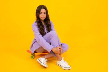 Poster - Teenager lifestyle. Beautiful and fashion teenager child girl in moder suit posing with a skateboard isolated on yellow background.