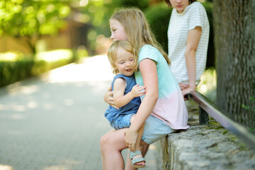 Sticker - Cute big sister cuddling with her toddler brother. Adorable teenage girl holding baby boy. Children with large age gap.