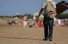 Peddler With Long Pants Walking On The Sunny Beach Looking To Sell Glasses