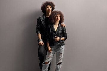 Sticker - Young man and woman with leather jackets and curly hair leaning on a gray wall