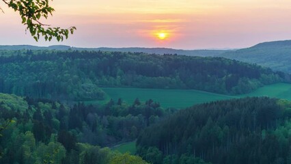 Wall Mural - Time lapse of sunset on a partly cloudy sky over rural landscape with meadows and forest of the Eifel, Germany