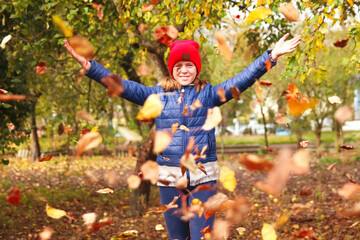 Defocus autumn people. Teen girl raising hand and throwing leaves. Many flying orange, yellow, green dry leaves. Enjoy autumn. Happy fall. Funny season. Smiling kid. Out of focus