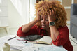 © AnnaStills - African exhausted woman holding her head while sitting at table with bills and taxes, she tired of counting and paying
