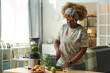 © AnnaStills - African young girl cutting vegetables for green smoothie at table in living room to drink it in the morning