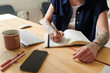 © AnnaStills - Close-up of woman making to-do list and writing it in her notepad while sitting at her workplace in the room
