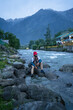 © 3 Travelers - A man sitting along on the Lidder River with his shoes, Pahalgam, Jammu and Kashmir, India.