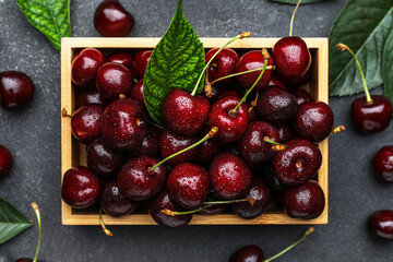 Wooden box with tasty cherries on dark background