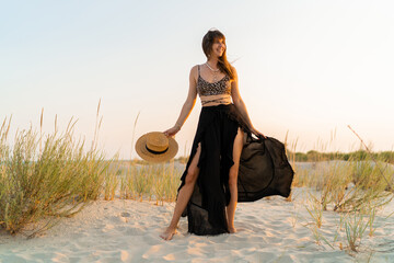 Wall Mural - Sexy  brunette woman in stylish summer  boho outfit posing on the beach.  Sunset colors.