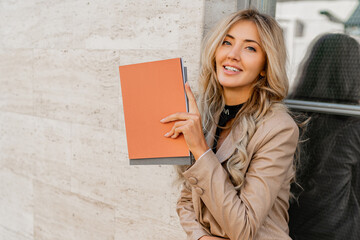 Wall Mural -  Close up photo of Elegant sucsessful blond  woman in stylish casual outfit posing   on the street. Holding advertising catalogs.