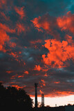 Fototapeta Sypialnia - Beautiful red cloudy sunset in evening. Silhouettes of trees and tower against sky