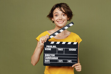 Wall Mural - Young surprised amazed happy woman she 20s wear yellow t-shirt holding classic black film making clapperboard isolated on plain olive green khaki background studio portrait. People lifestyle concept.