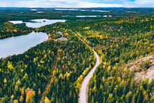 Aerial View Of Rural Road In Yellow And Orange Autumn Forest With Blue Lake In Finland