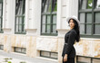 © Yuliia - Tall modern girl in black jacket stands near the entrance to the office build