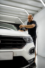 Man polishing a white car, wearing a black t-shirt