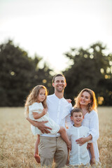 beautiful young family at sunset in a wheat field. happy parents with two children, a boy and a girl