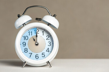 Fototapete - Eleven o'clock on the alarm. A white alarm clock is on a white table. The clock hand points to 11 o'clock. Time to change to summer or winter time. Set an alarm for 11:00 or 23:00. copy space