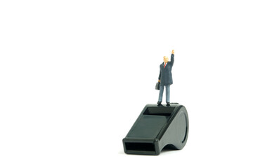 Miniature people toy figure photography. Whistle blower concepts. A businessman standing above black whistle while raise his hand. Isolated on white background