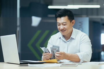 Wall Mural - Successful asian investor counting dollars money cash sitting in office, happy man smiling and happy