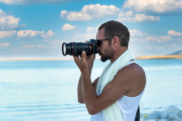 Man photographer takes photographs with dslr camera at the beach. Travel, vacations, professional freelance work, active lifestyle concept. Handsome muscular man using picture with modern camera