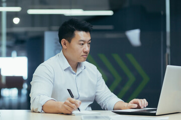 Wall Mural - Serious and focused asian male accountant working with documents in modern office, businessman behind paper work