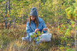 Seasonal berries picking. Young woman in hipster hat on swamp searching for ripe cranberries. Happy female in 20s spend weekend outside city in autumn forest relaxing and recreating in nature alone