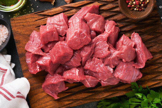 Raw chopped beef meat. Raw organic meat beef or lamb, spices, herbs on old wooden board on dark grey concrete background. Goulash. Raw uncooked meat. Meat with blood. Top view with copy space.