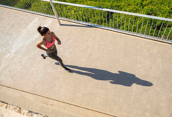 Side view of young woman running on sidewalk in morning. Health conscious concept with copy space.